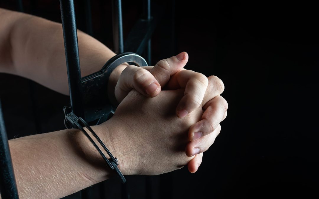 Prisoner in handcuffs praying, prisoner prays in a cell behind bars
