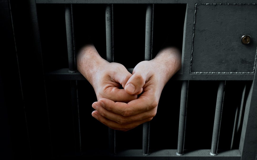 A closeup of a dimly lit prison holding cell door with arms reaching out in a folded position